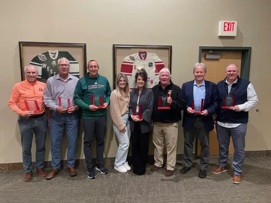 Eight award recipients holding their plaques in front of framed jerseys at a Minnesota hockey banquet, 2023