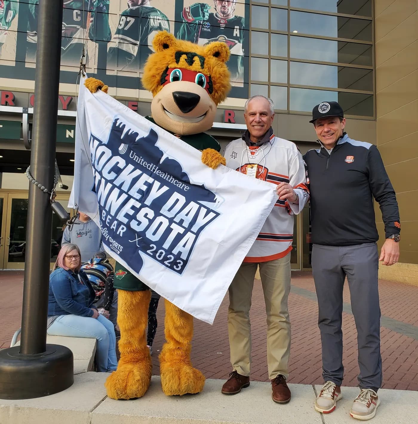 Holding the Hockey Day Minnesota 2023 flag outside the arena with the Minnesota Wild mascot