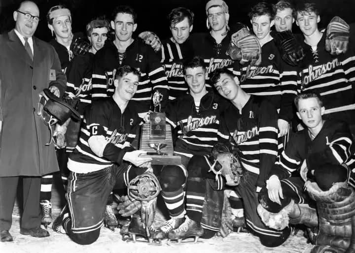 Black and white team photograph of a St. Paul Johnson high school hockey team posed on the ice around a championship trophy